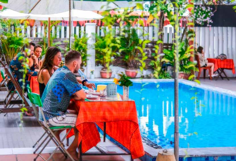 Mesas con personas desayunando en la piscina de Oleander Homestay, una excelente opción para dormir barato en Hoi An